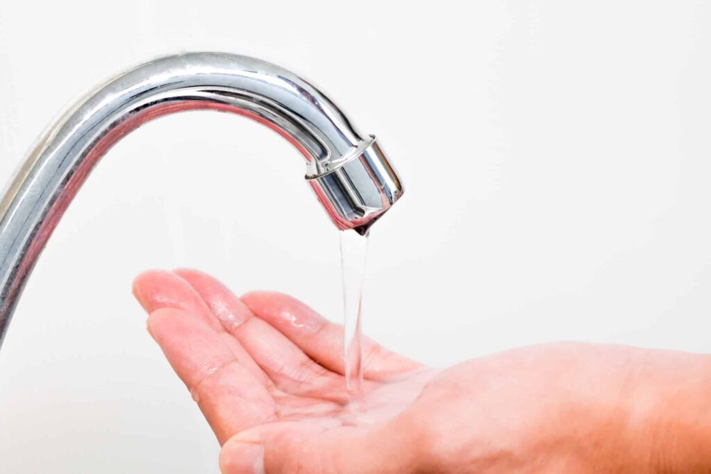 a hand catching water that's falling from a silver sink faucet