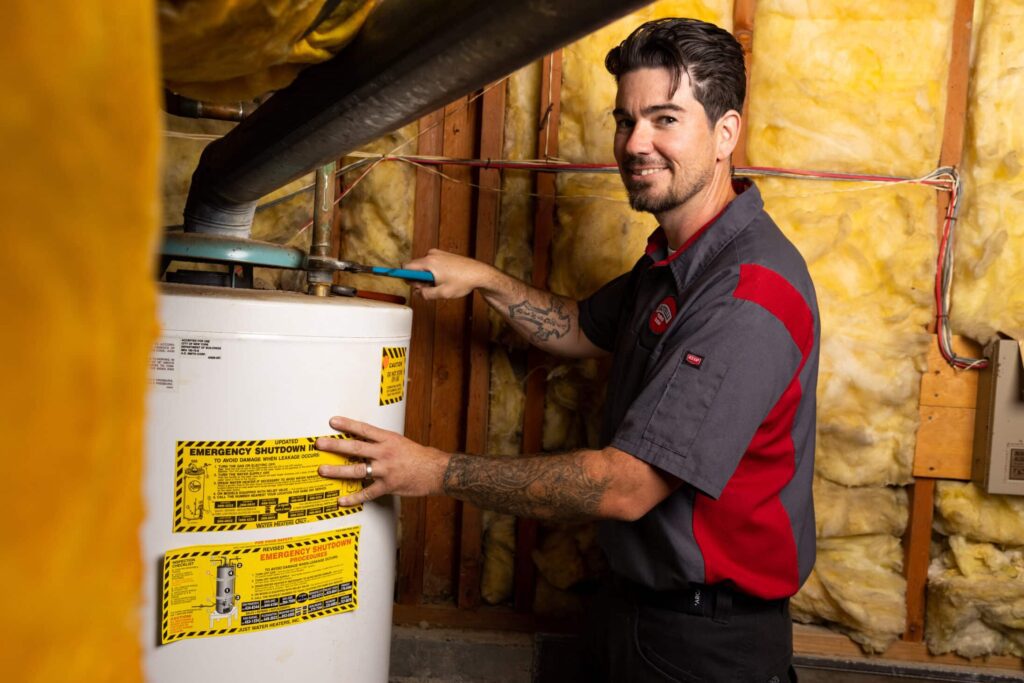 a Gotelli plumber smiling while using a wrench to adjust a tanked water heater