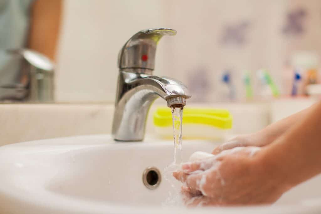 hands with soap suds being washed under a faucet with clean water running